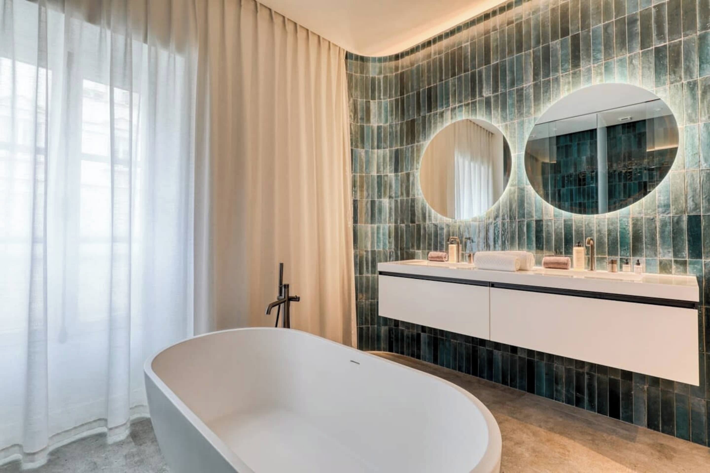 Un baño moderno con una bañera independiente, un tocador con espejo y una pared de azulejos.