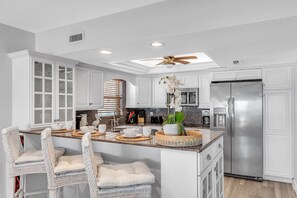 A kitchen with white cabinetry, a stainless steel refrigerator, and a central island with bar stools.