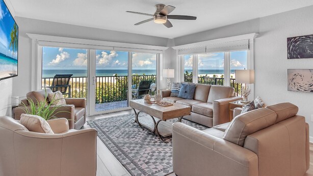 A spacious living room with a large window overlooking the ocean, a ceiling fan, and a view of the beach. - Premium Beachfront, Spectacular Views, Walk to Pier 60, Free Parking! ~ 201 Surfside (Clearwater)