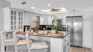 A modern kitchen with white cabinetry, a stainless steel refrigerator, and a central island with bar stools. - Premium Beachfront, Spectacular Views, Walk to Pier 60, Free Parking! ~ 201 Surfside (Clearwater)