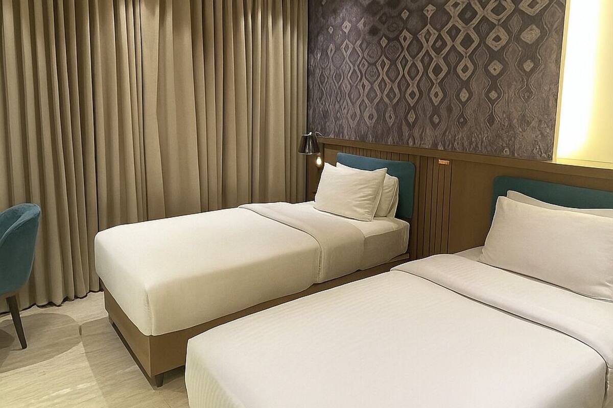 A hotel room with two beds, a large window with curtains, a ceiling fan, and a patterned wall.