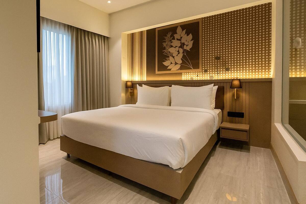 A modern hotel room with a large bed, a bedside table, a lamp, and a decorative wall panel.