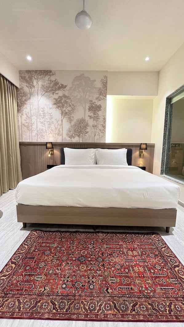 Una camera d'albergo con un letto grande, un tappeto decorato, una parete con un affresco di un albero e una finestra con vista.