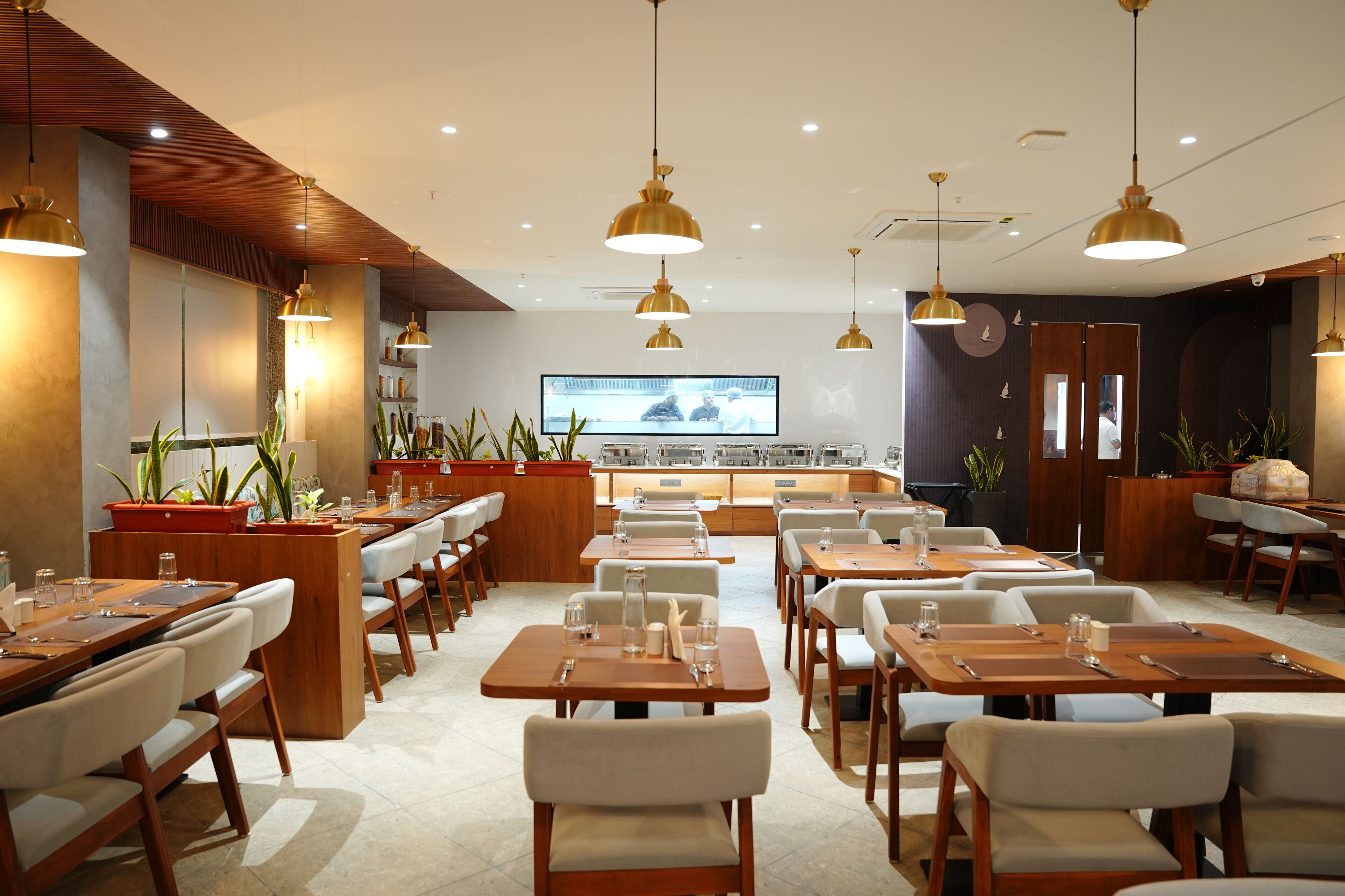 A restaurant with multiple tables and chairs, pendant lighting, and potted plants.