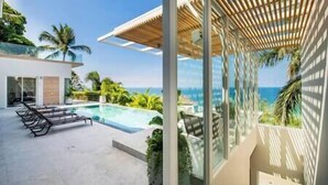 Un espace piscine extérieur moderne, doté de chaises longues, d’une pergola et offrant une vue sur l’océan.
