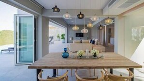 Un espace de repas moderne avec une table et des chaises en bois, des luminaires suspendus et une vue sur l’extérieur.