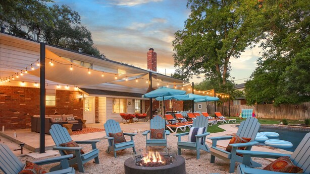 Eine Terrasse im Freien mit Adirondack-Stühlen, einer Feuerstelle und Lichterketten.