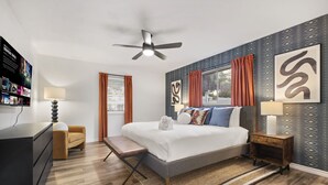 Ein modernes Schlafzimmer mit Bett, Nachttischen, einer Bank, einem Schreibtisch und einem Deckenventilator.