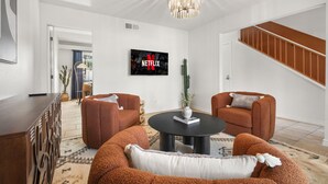 Ein modernes Wohnzimmer mit einem schwarzen Couchtisch, zwei braunen Sofas und einem an der Wand befestigten Fernseher, der das Netflix-Logo zeigt.