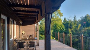 A covered patio with a table and chairs, a wooden deck, and a view of a forested area. - Half of a Holiday Home, Huge Garden, Pond (gmina Stężyca)