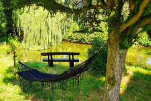 A hammock tied to a tree, a wooden bench, and a pond in a natural setting.