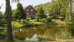 Una casa con uno stagno antistante, circondata da alberi e un piccolo gazebo.