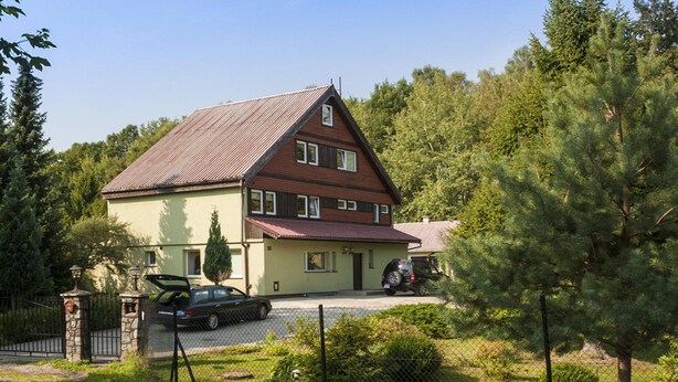 Una casa a due piani con tetto spiovente, vialetto recintato e un'auto parcheggiata.