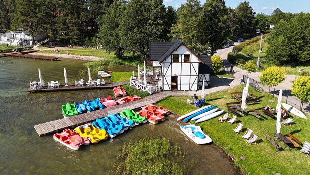 A lakeside lodge with a dock, colorful inflatable boats, and outdoor seating. - Half of a Holiday Home, Huge Garden, Pond (gmina Stężyca)