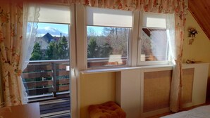 Una stanza con soffitto spiovente, una panca in legno, un termosifone e una finestra vista alberi e un edificio.