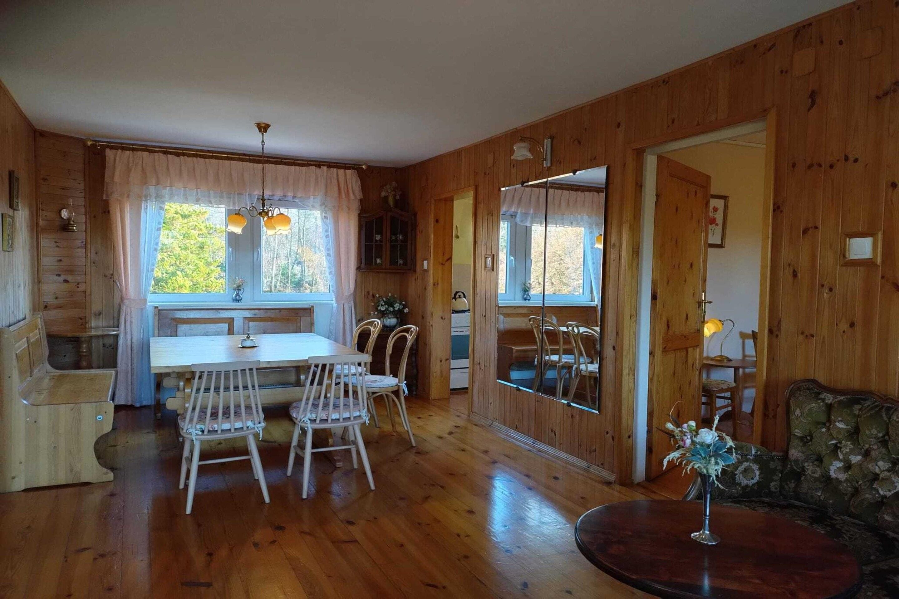 A wooden interior with a dining table, chairs, a sofa, and a small table with a vase.