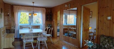 A wooden interior with a dining table, chairs, a sofa, and a small table with a vase.