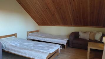 A small, single-room accommodation with two wooden beds, a sofa, and a table.