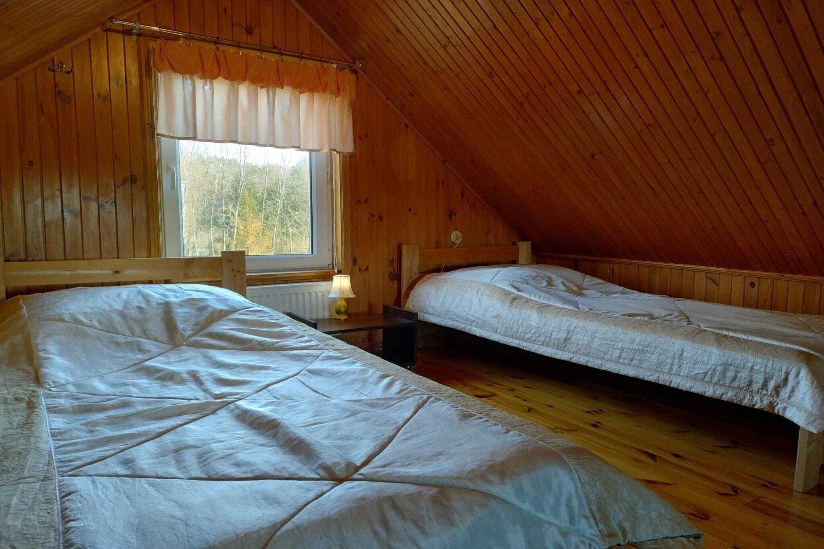 Una habitación con dos camas, paredes de madera, una ventana con cortinas y techo inclinado.