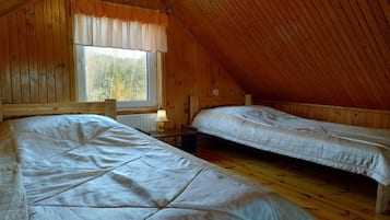 Ein Zimmer mit zwei Betten, Holzwänden, einem Fenster mit Vorhängen und einer geneigten Decke.