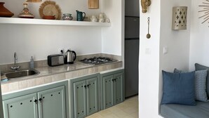 Une cuisine moderne équipée d’une cuisinière à gaz, d’un évier et d’un grille-pain. On peut y admirer des objets décoratifs, notamment un tajine marocain et un panier tressé, qui sont disposés sur les étagères.