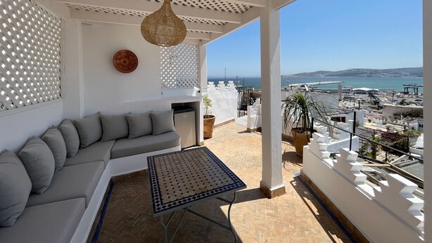 Un balcon avec un canapé blanc, une table à motifs et une vue sur la mer et le paysage urbain.