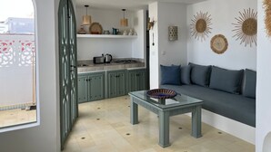 Une cuisine moderne avec des meubles de rangement verts, une table à plateau en verre et un canapé avec des coussins bleus.