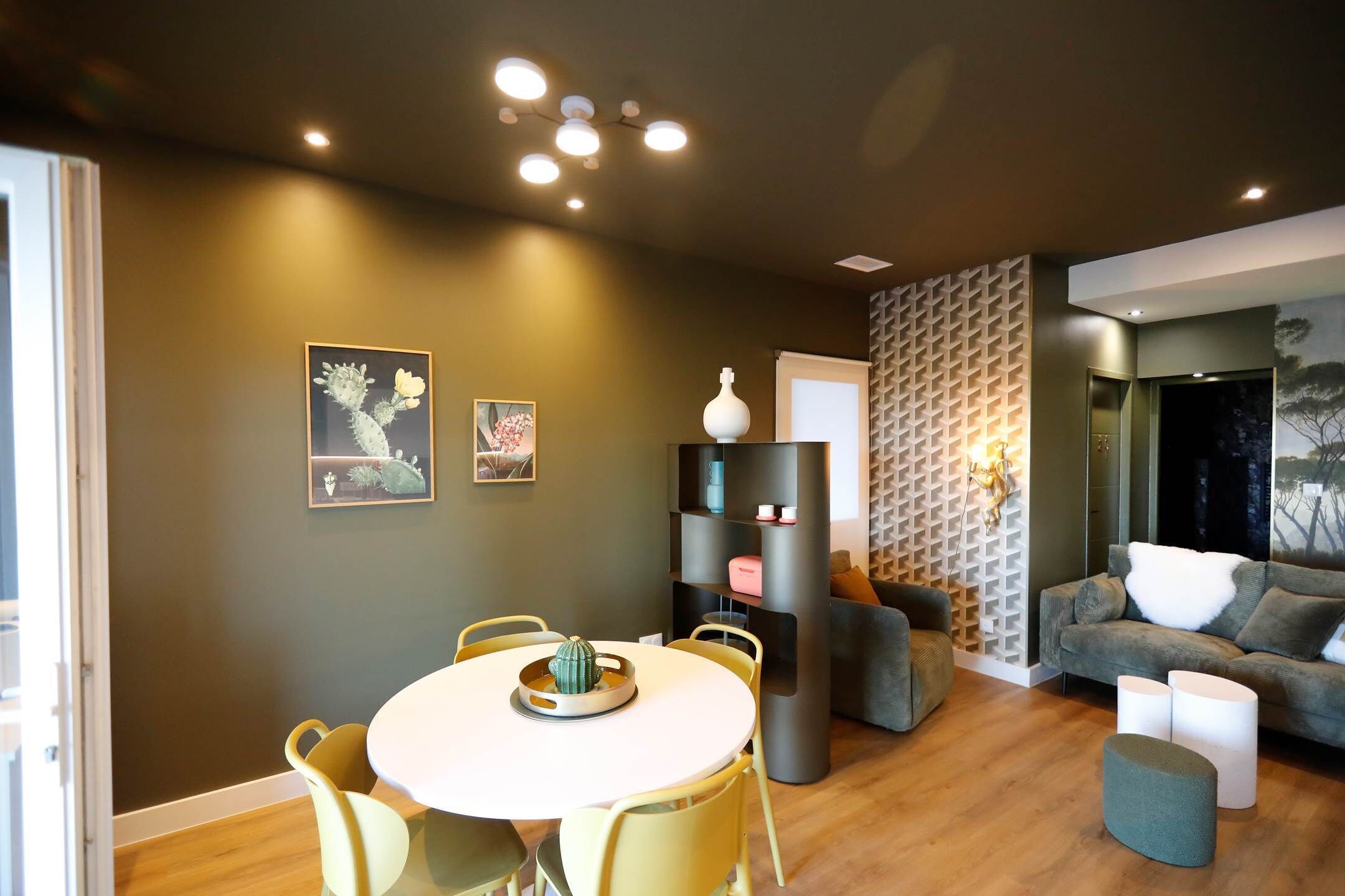 Ein modernes Wohnzimmer mit einem runden Esstisch, gelben Stühlen, einem grauen Sofa und einer Wand mit Muster.