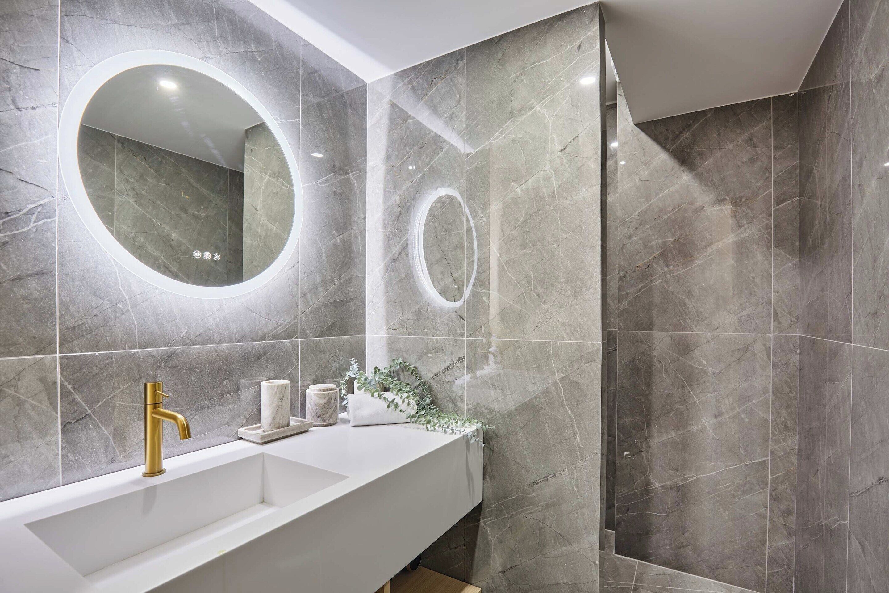 A modern bathroom with a white vanity, gold faucet, and marble tiles.