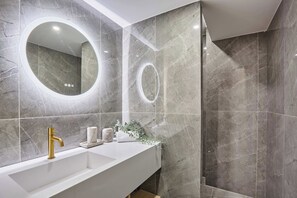 A modern bathroom with a white vanity, gold faucet, and marble tiles.