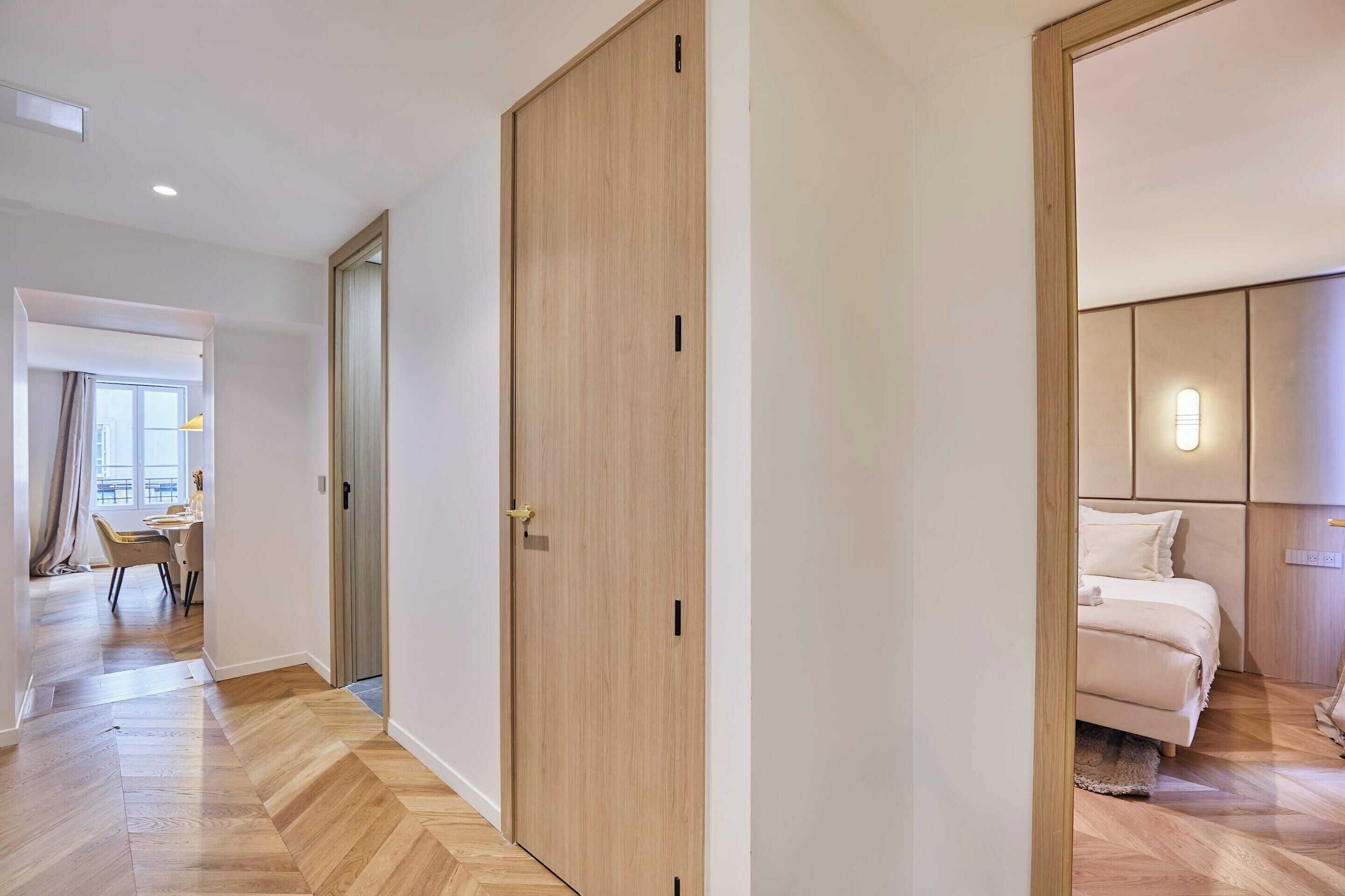 A hotel room with a wooden floor, a bed with a headboard, a nightstand, and a window.