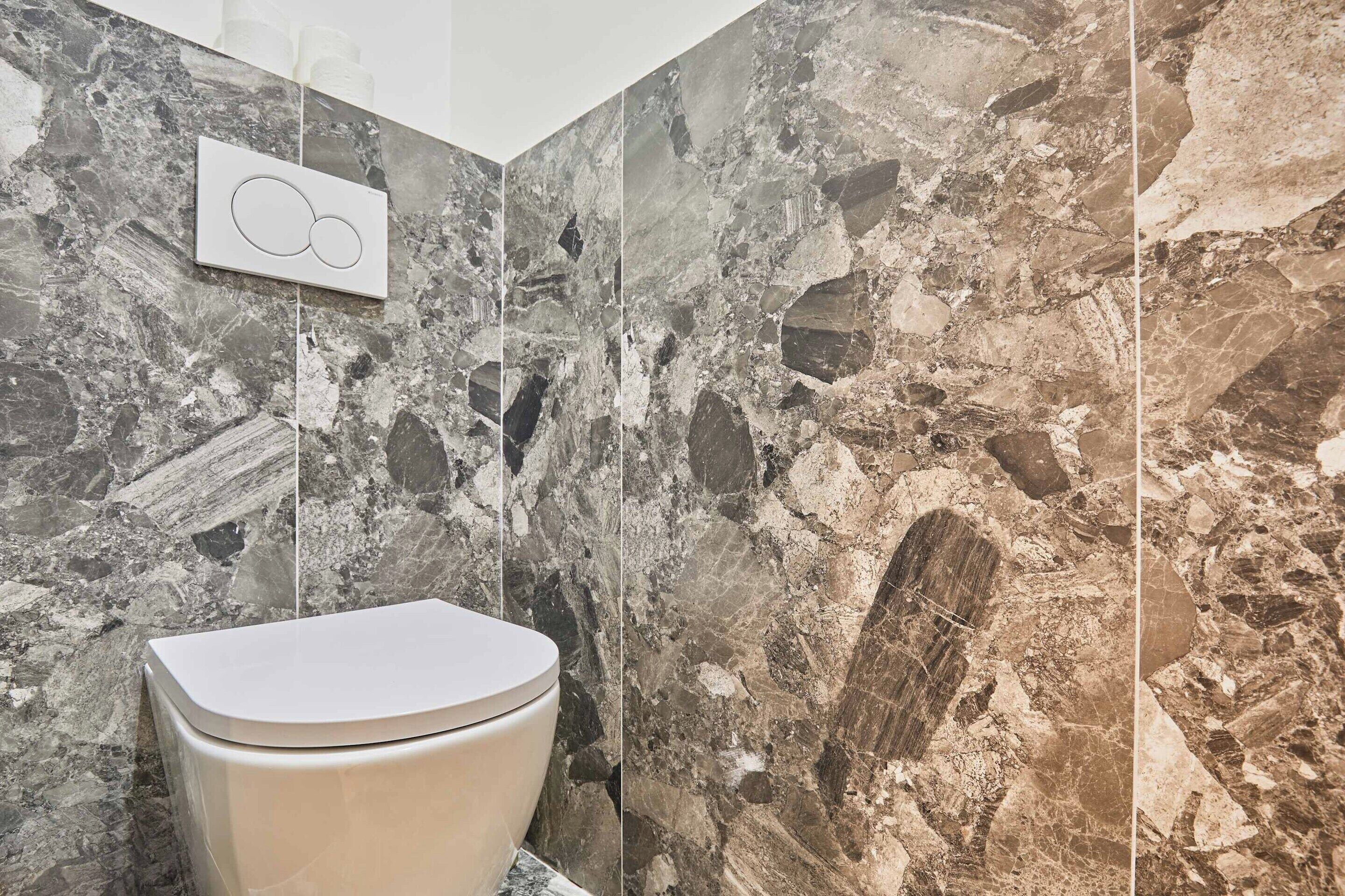 Une salle de bain avec des toilettes, des murs en marbre et un luminaire fixé au mur.