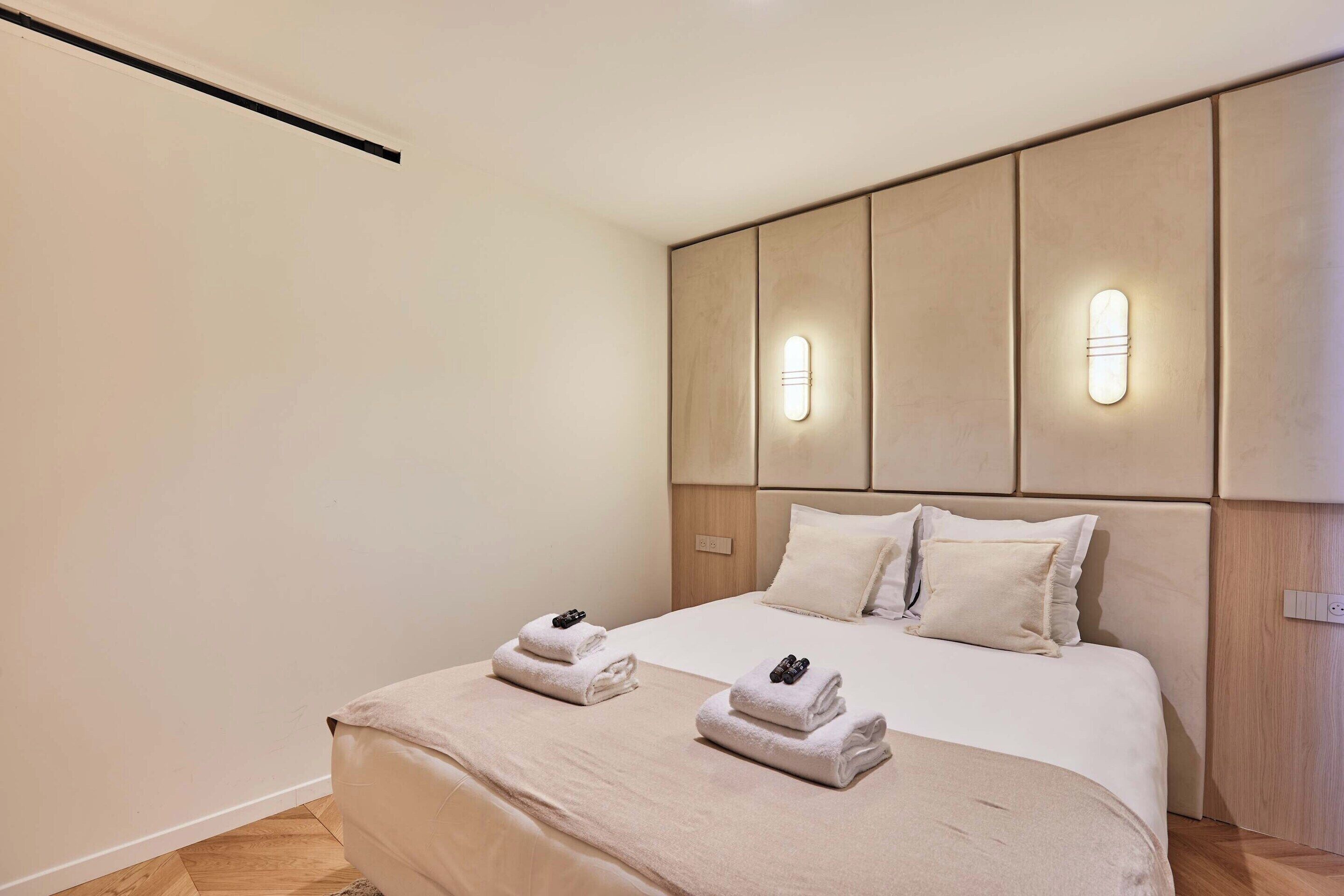 Et moderne hotelværelse med en stor seng, to sengeborde og en sengegavl med indbygget belysning.