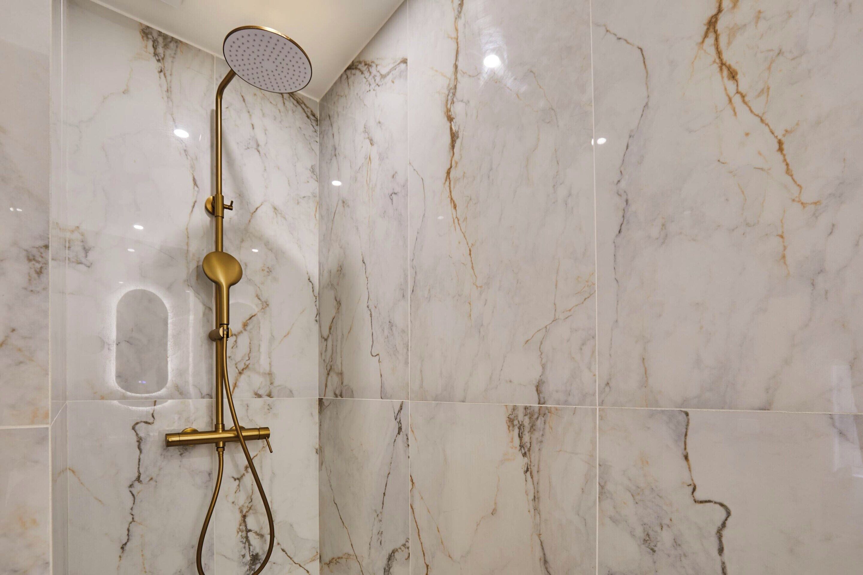A shower with a gold fixture and marble tiles.