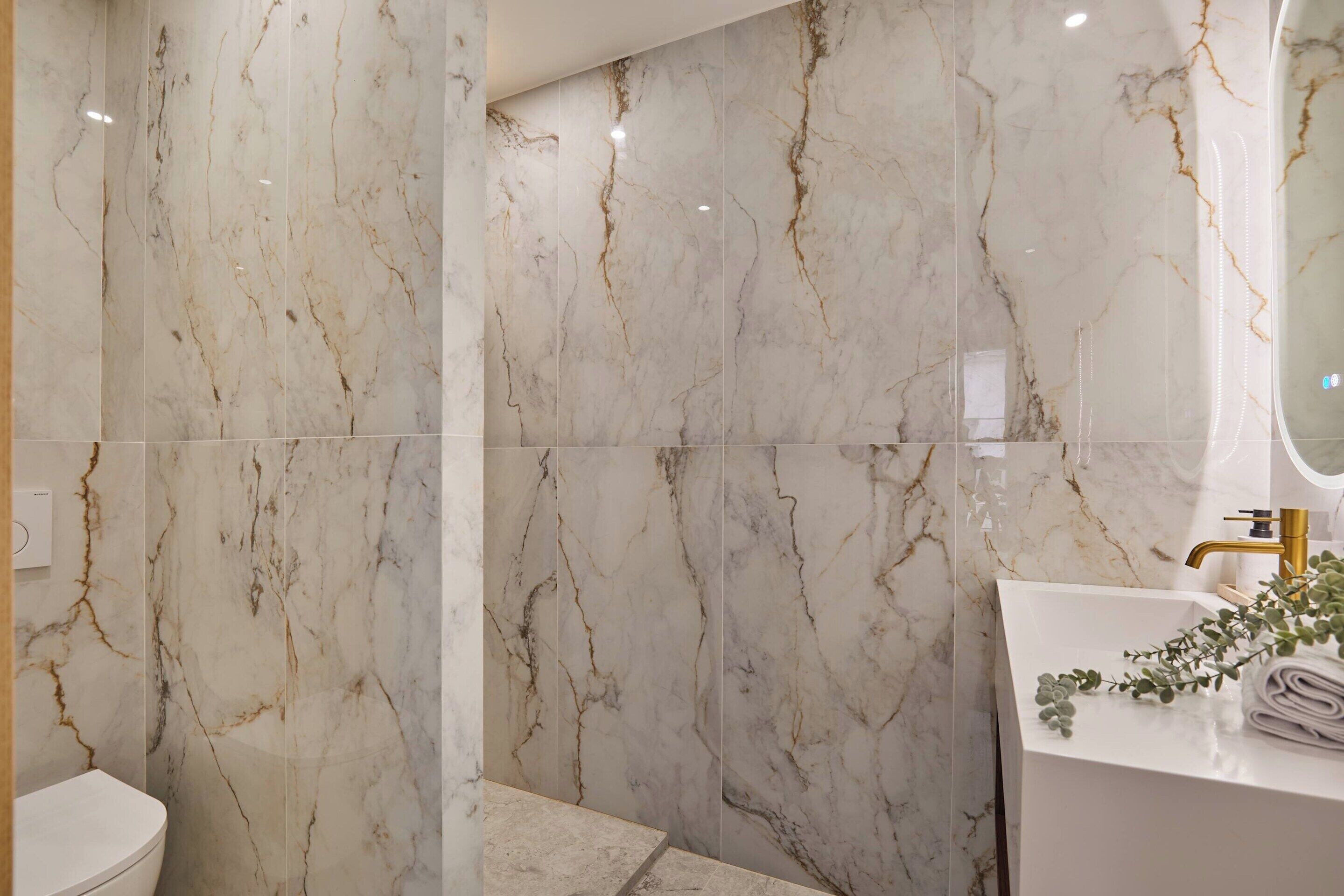 Un baño con paredes de mármol y un lavamanos blanco con detalles dorados.
