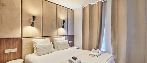 A modern hotel room with a large bed, a bedside table, and a wall-mounted light fixture.