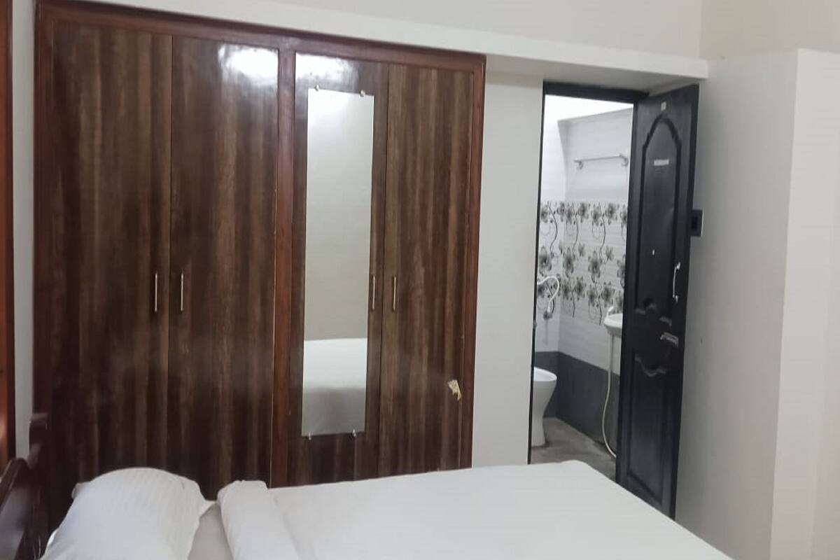 A bedroom with a wooden wardrobe, a bed, and a bathroom visible through an open door.