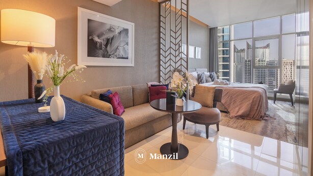 A modern hotel room with a sofa, a round table, a bed, and a large window offering a city view. - Manzil-Waterfront Studio in Business Bay (Dubai)