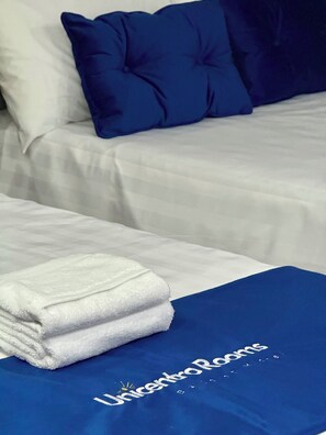 Un lit bien fait, avec du linge de lit blanc et une couverture bleue ornée du logo « UnicentroRooms ».
