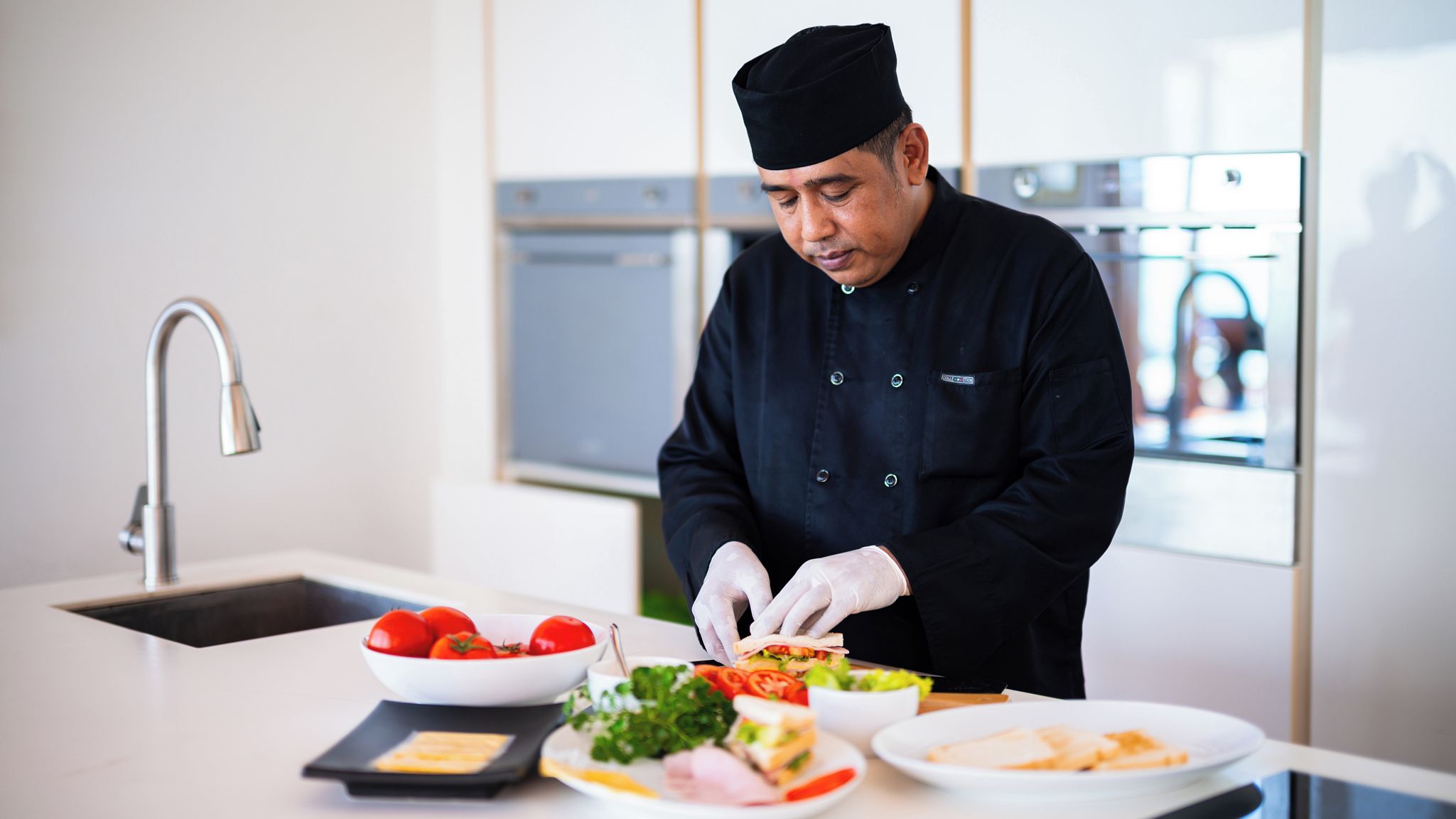 Un chef prépare un plat dans une cuisine moderne équipée d’appareils électroménagers en acier inoxydable et dotée d’un plan de travail blanc.