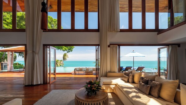 A spacious living area with a large sofa, a coffee table with a floral centerpiece, and a view of the ocean through large windows.