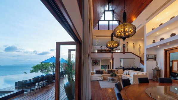 A spacious living area with a large wooden table, comfortable seating, and a view of the sea.