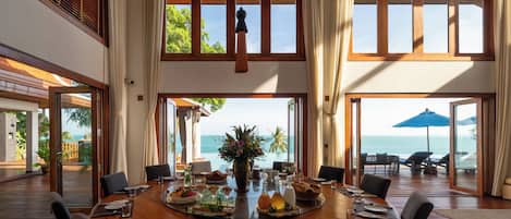 A spacious dining area with a view of the ocean, large windows, and a ceiling fan.