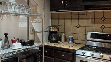 Una cocina con armarios de madera oscura, una estufa de acero inoxidable y un horno empotrado. Hay repisas con cristalería y una cafetera en la encimera.