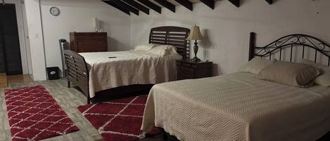 A bedroom with two beds, a wooden floor, a red rug, a ceiling fan, and a clock on the wall.