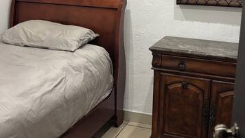 A bedroom with a wooden bed, a small wooden dresser, and a mirror on the wall.
