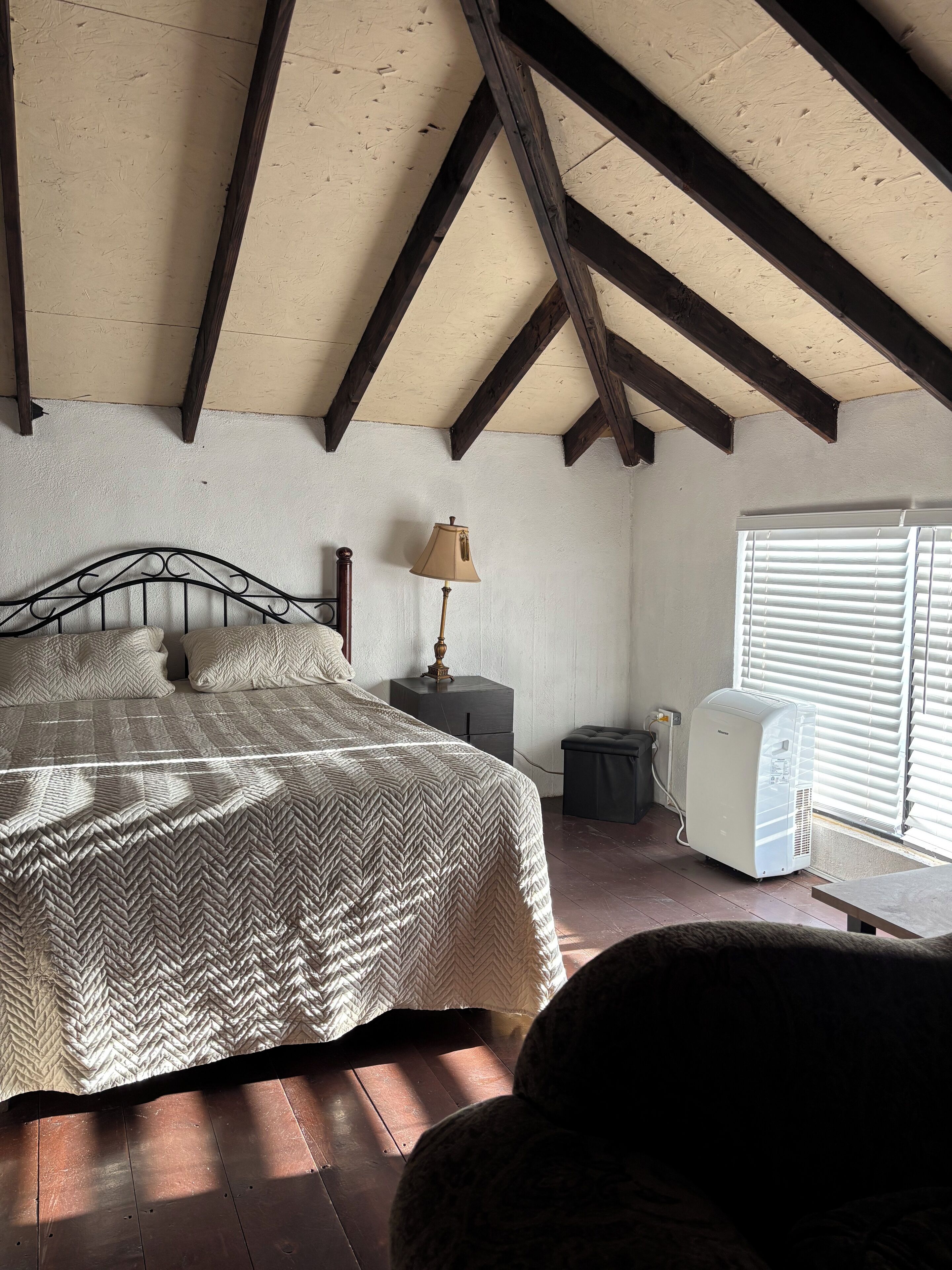 Un dormitorio con cama, lámpara de noche y ventana con persianas.