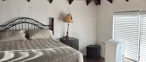 Un dormitorio con cama, lámpara de noche y ventana con persianas.