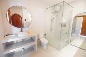 A modern bathroom with a glass-enclosed shower, a round mirror, a sink, and a toilet. - Pulestis Glamping (Kintamani)