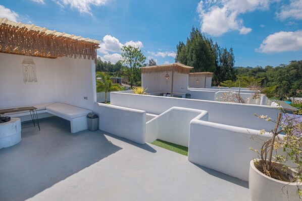 A rooftop terrace with white walls, a seating area, and a small garden.